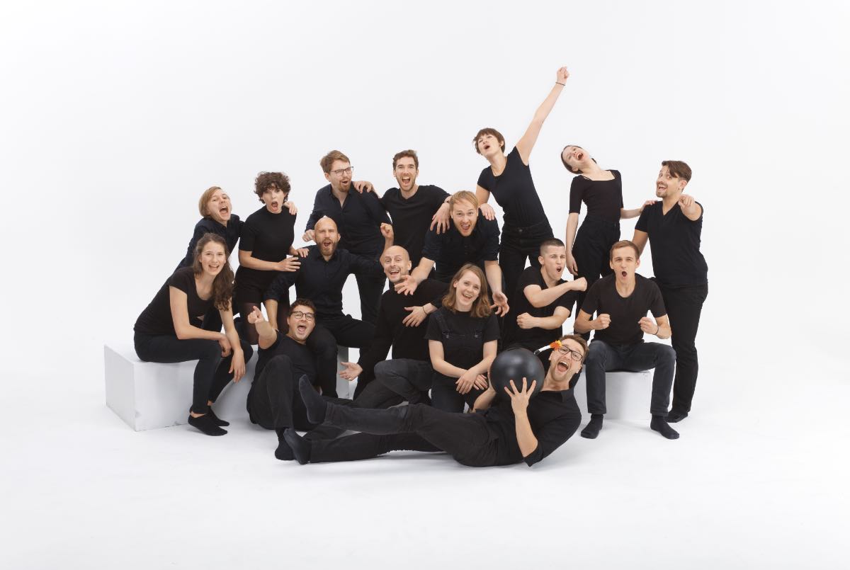 Das Ensemble des Improtheaters Kanonenfutter, schwarz gekleidet, in ausgelassenen Posen vor weißem Hintergrund